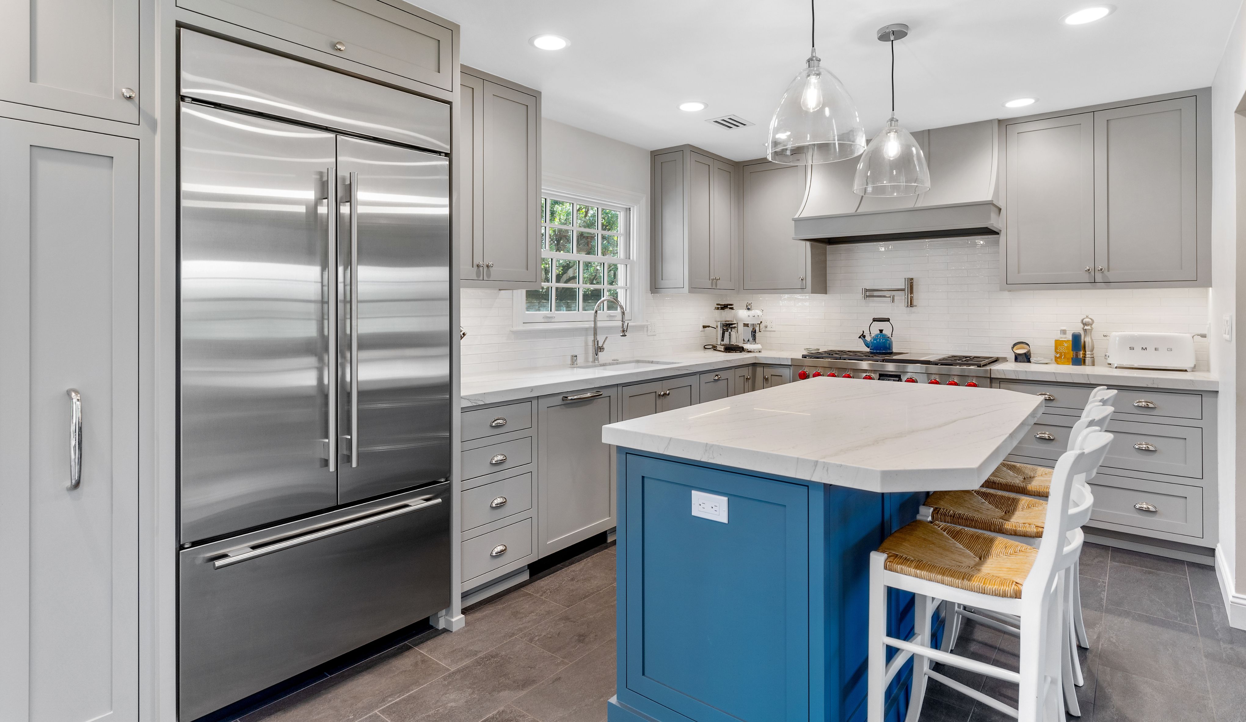 Del Mar kitchen remodel with custom gray hood, stainless range, white tile backsplash and blue island cabinetry.
