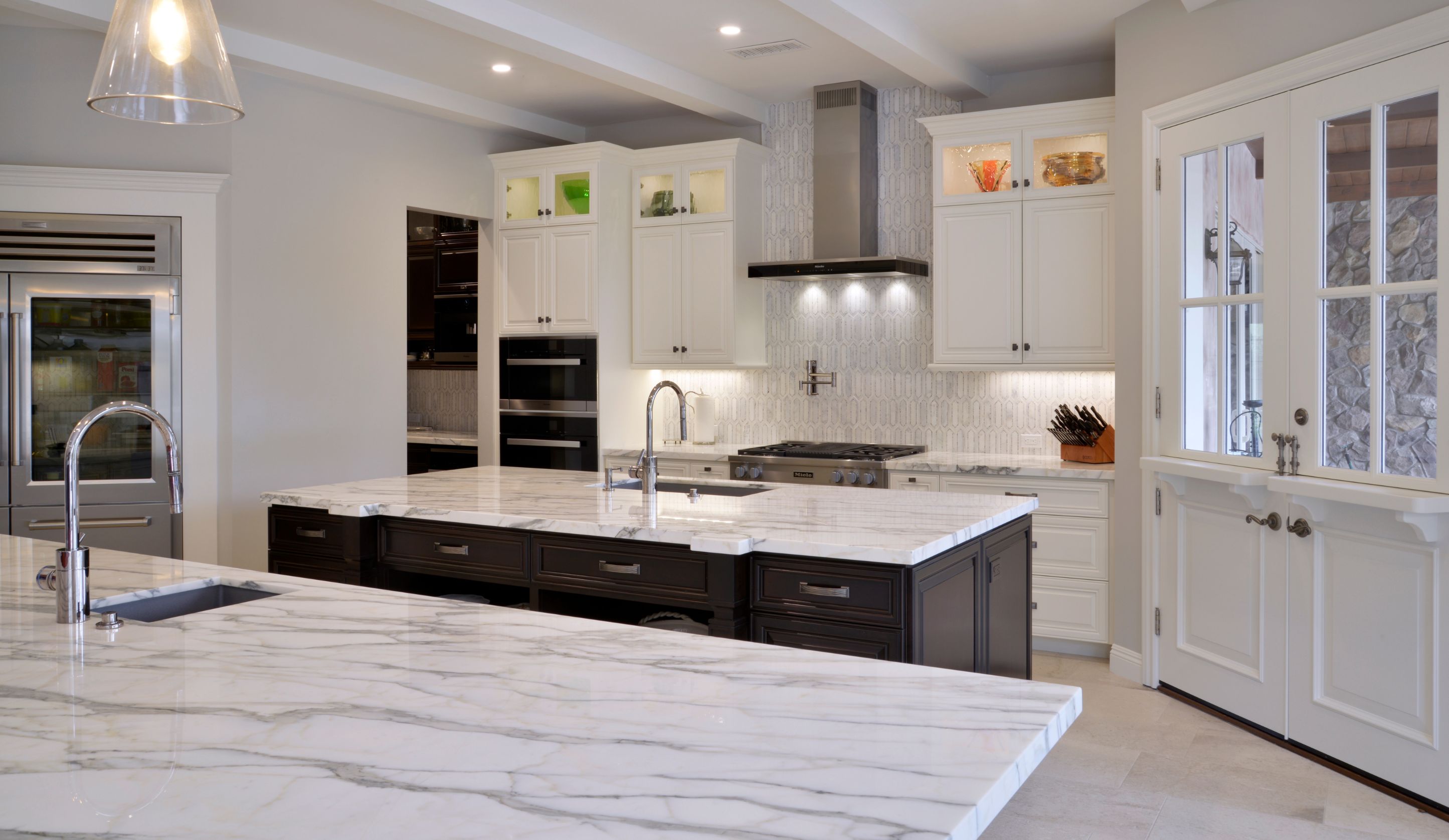 Del Mar remodeled kitchen with large dark island, white cabinetry, marble-look counters, stainless appliances and French doors.