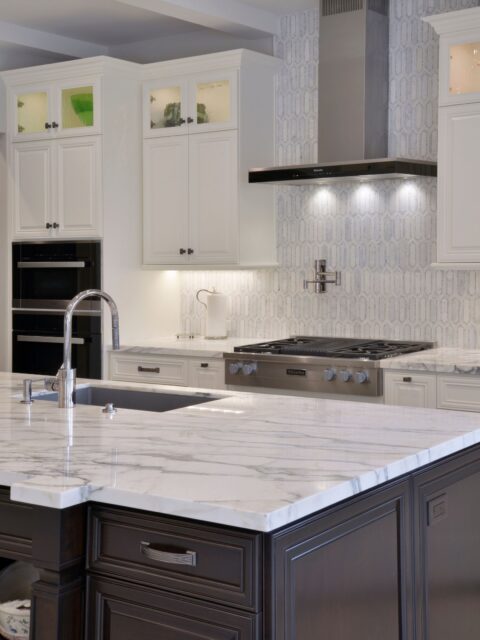Del Mar kitchen remodel with dark island cabinetry, marble-look counters, white cabinets, stainless cooktop and geometric backsplash.