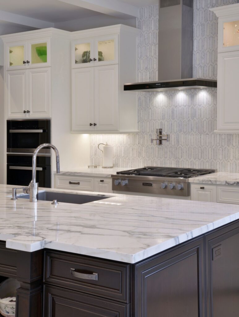 Del Mar kitchen remodel with dark island cabinetry, marble-look counters, white cabinets, stainless cooktop and geometric backsplash.