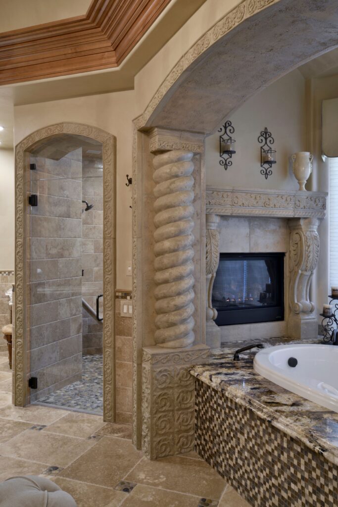 Bathroom shower and tub area with carved stone arches, spiral column, fireplace, granite surround and mosaic tile.