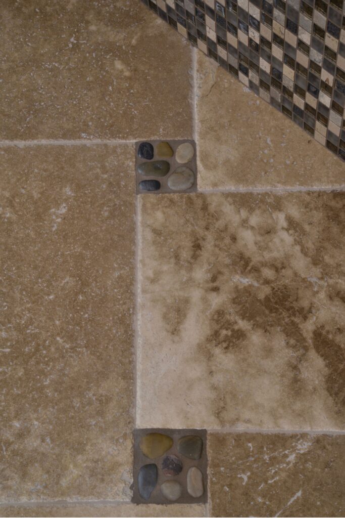 Stone bathroom floor with pebble accent insets and coordinating square mosaic tile along the adjacent wall.
