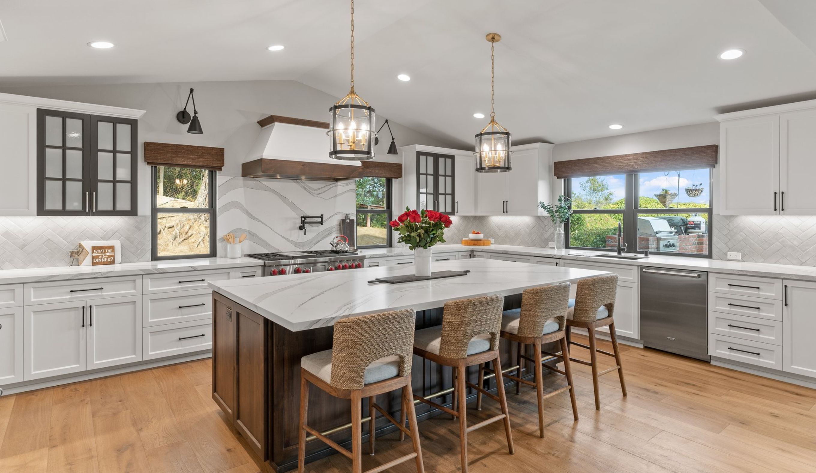 Wide view of Encinitas remodeled kitchen with large seating island, white cabinetry, wood flooring and vaulted ceiling.