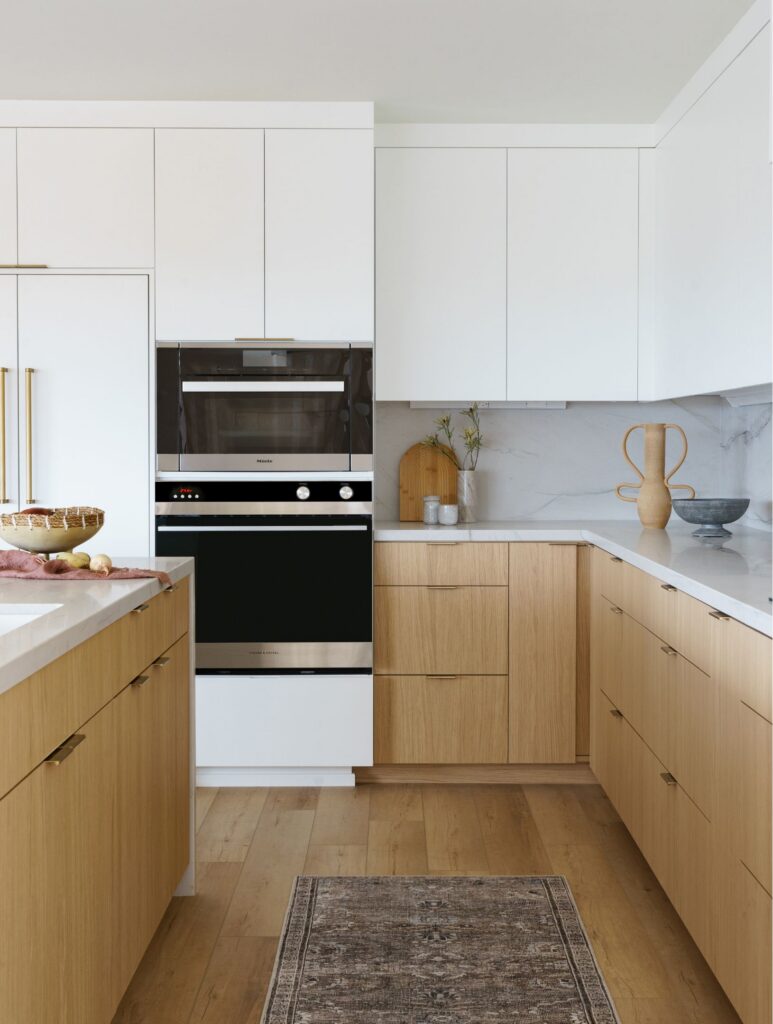 Escondido whole-home remodel kitchen with light wood cabinetry, white uppers, stacked ovens and veined stone countertops