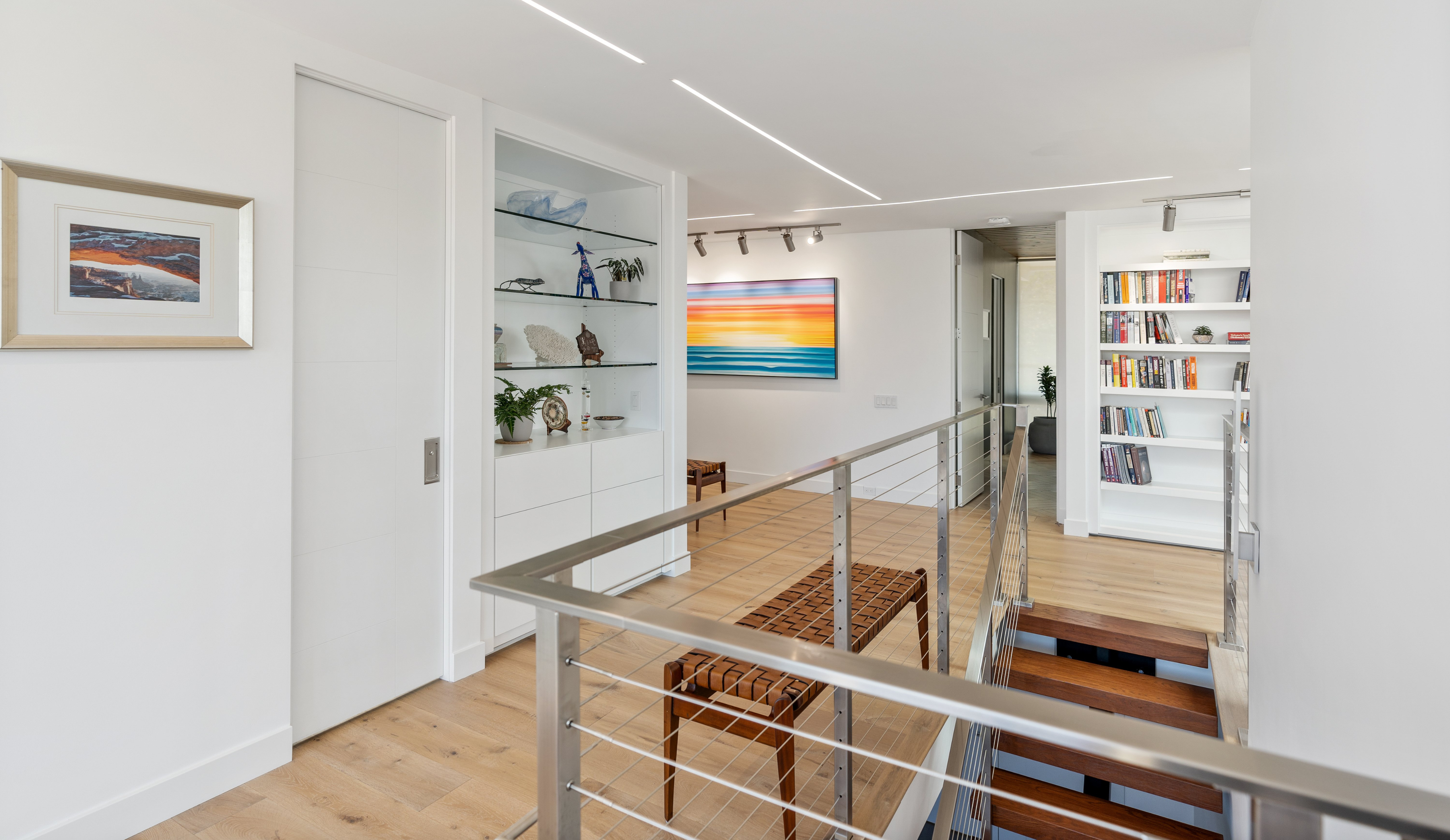 Upper landing in an Escondido whole-home remodel with cable railing, built-in shelving, wood floors and linear ceiling lights.