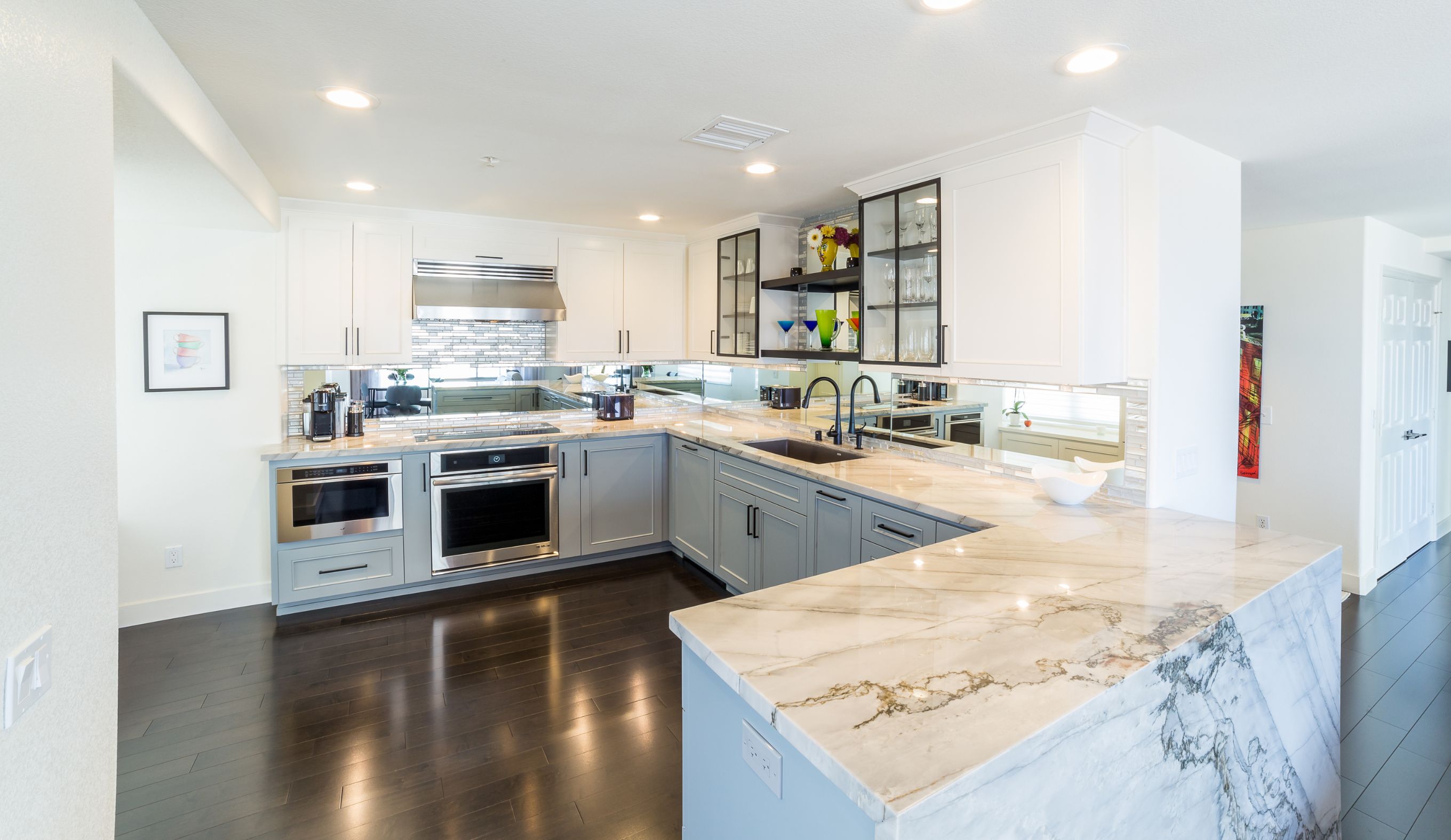San Diego kitchen remodel with two-tone cabinetry, veined waterfall countertop, mirrored backsplash and dark wood flooring.