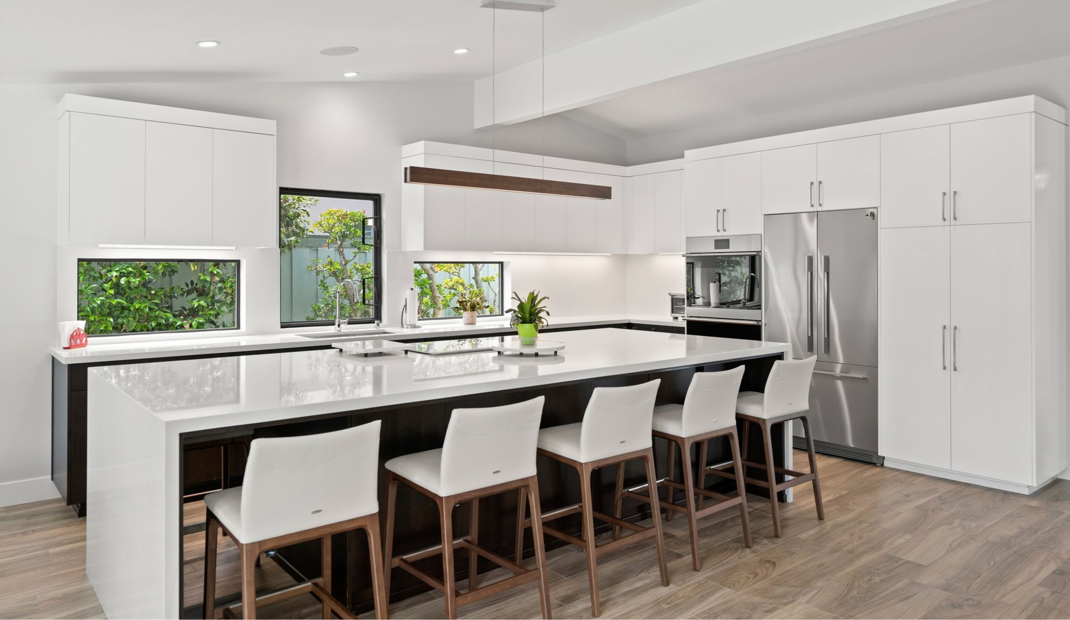 San Diego interior remodel with open kitchen, large white island, two-tone cabinetry, stainless appliances and black-framed windows.
