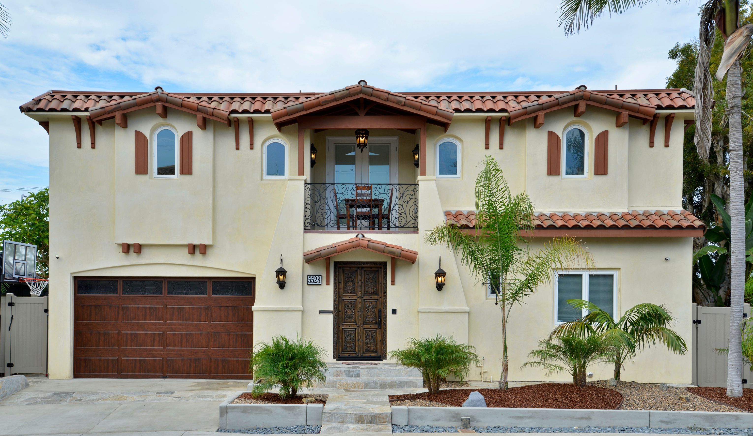 La Jolla remodeled entry with carved wood double doors, wrought-iron balcony, clay tile roof and arched windows.