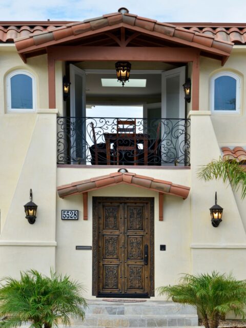 Two-story La Jolla whole-home remodel with stucco exterior, clay tile roof, arched windows, wood garage door and balcony.