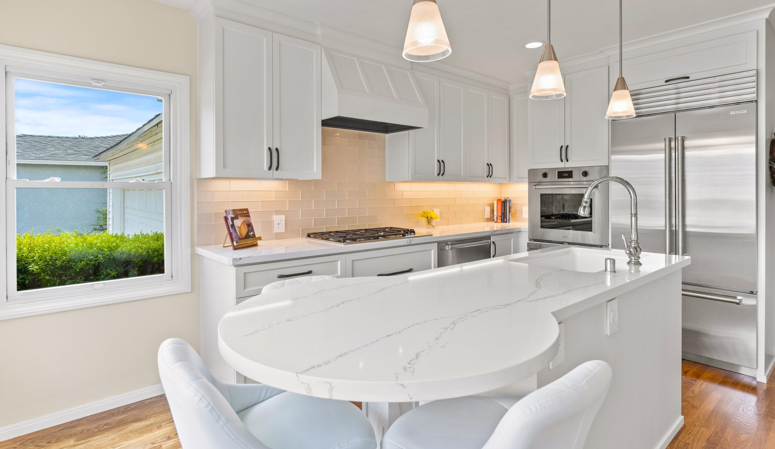La Mesa remodeled kitchen with curved island seating, white cabinetry, pendant lights, stainless appliances and wood floors.