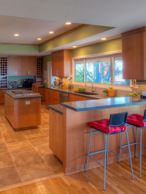 La Mesa kitchen remodel with wood cabinetry, cooktop island, bar seating, gray counters, tile flooring and wide sink window.