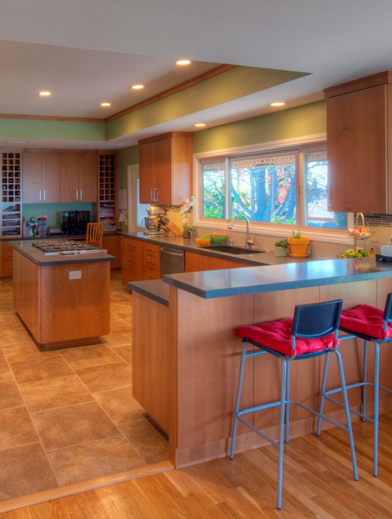 La Mesa kitchen remodel with wood cabinetry, cooktop island, bar seating, gray counters, tile flooring and wide sink window.