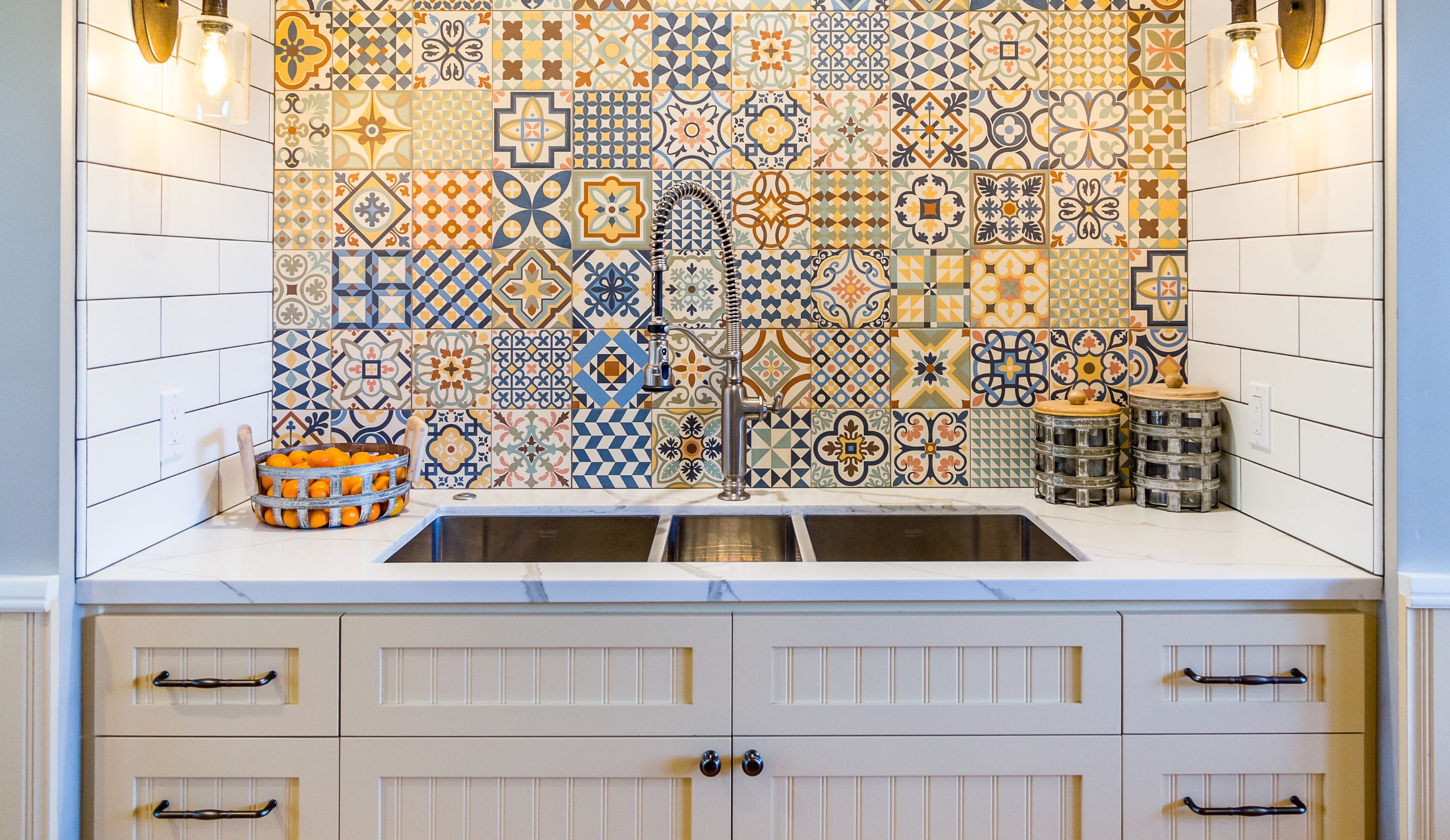 National City kitchen sink wall with colorful patterned tile, cream cabinetry, white counters and spring-coil faucet