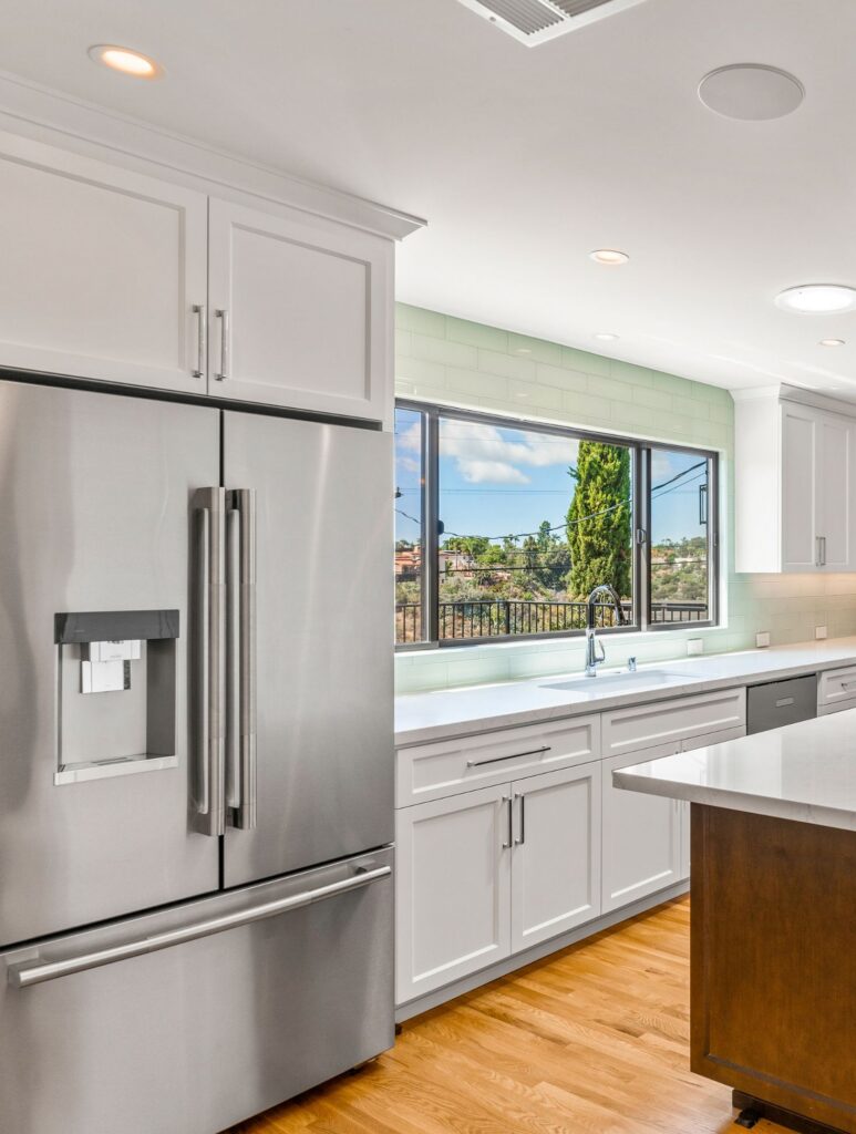 San Diego whole-home remodel kitchen with white shaker cabinetry, stainless refrigerator, green tile backsplash and large sink window