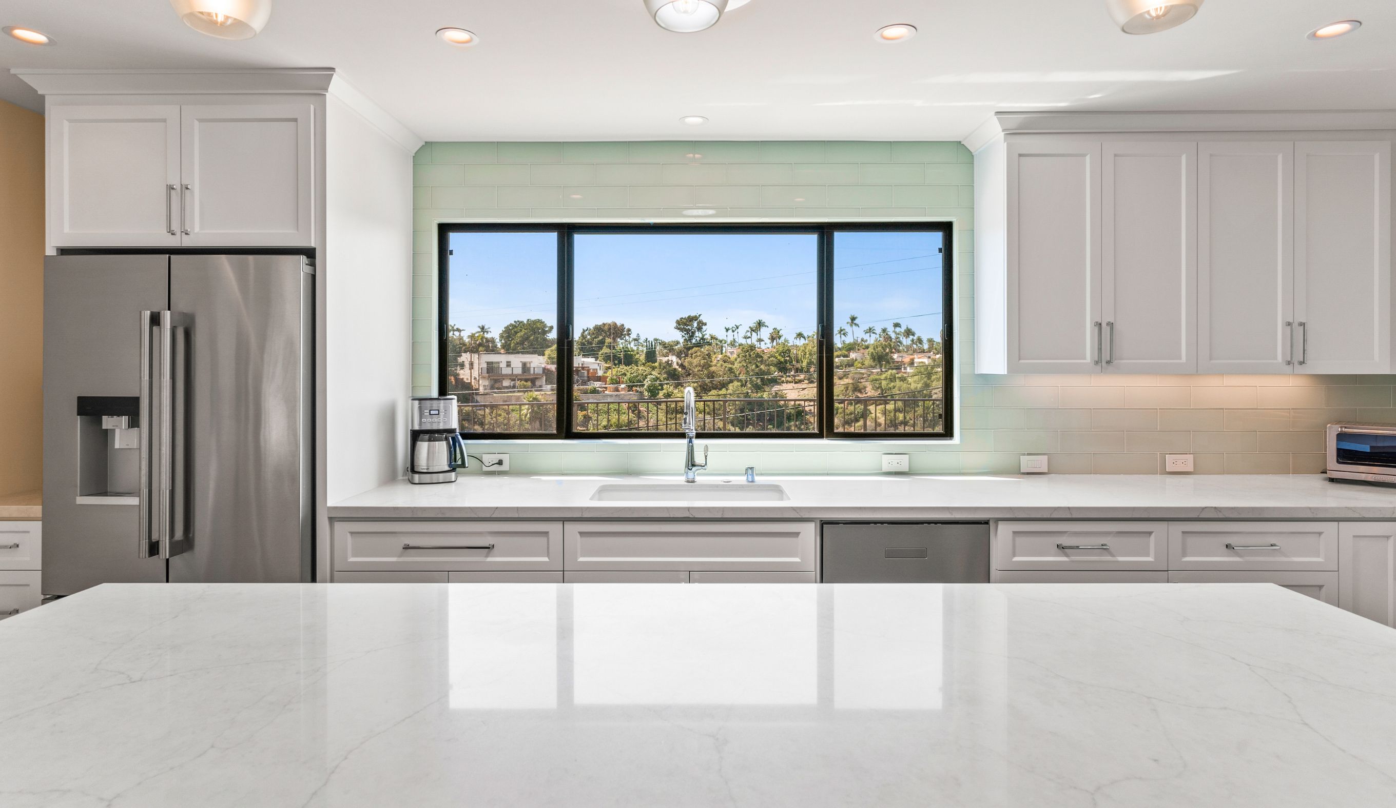 Remodeled San Diego kitchen with large island, white cabinetry, stainless appliances and wide canyon-facing window