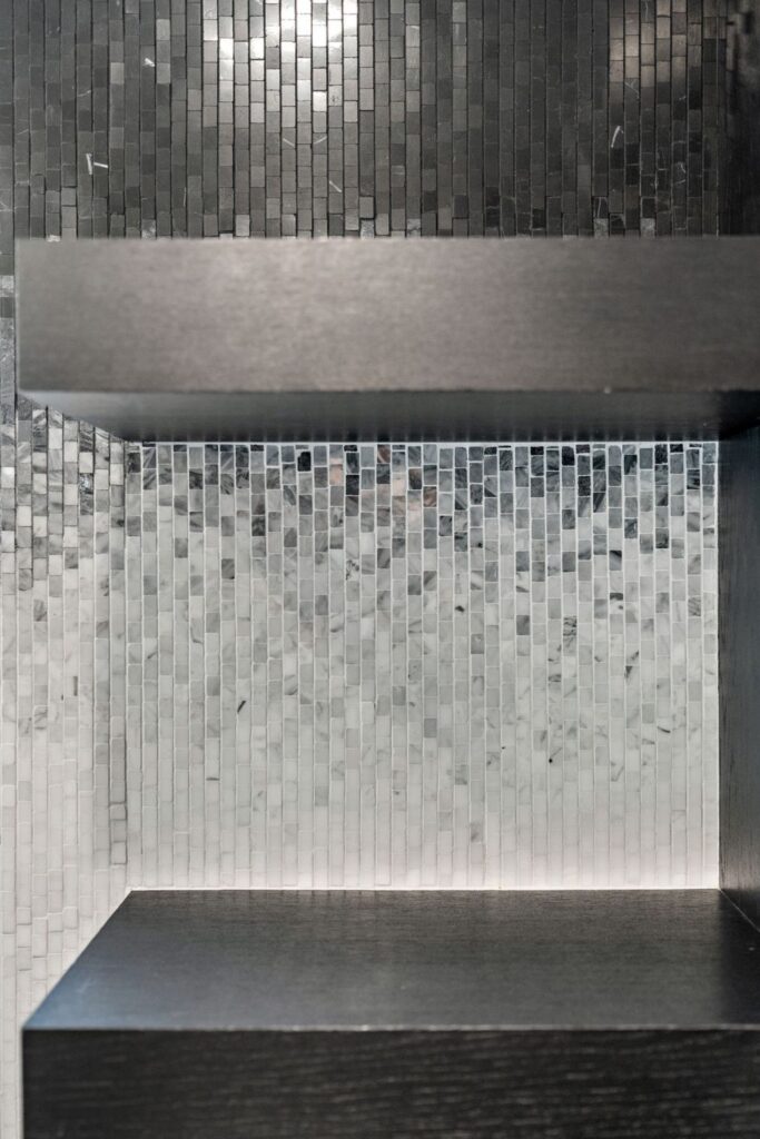 Black and white mosaic tile backsplash with dark floating shelf and textured vertical tile pattern