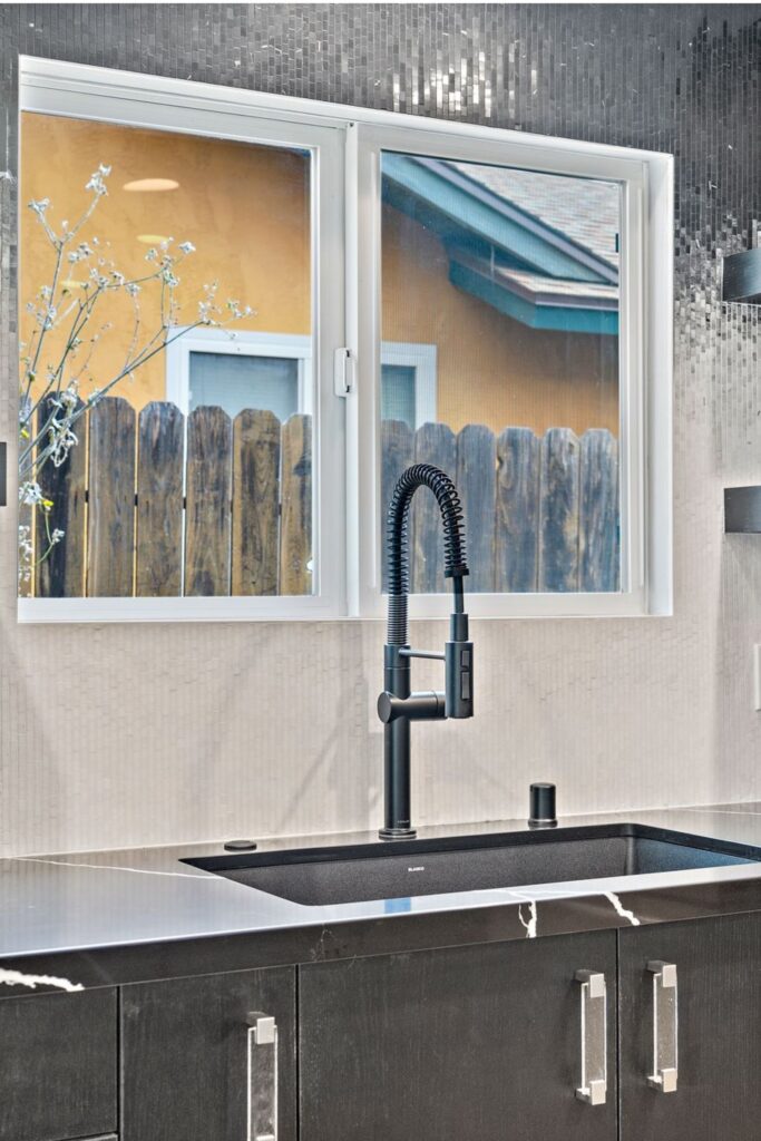 Kitchen sink with black spring faucet, dark cabinetry, black veined countertop and mosaic tile backsplash