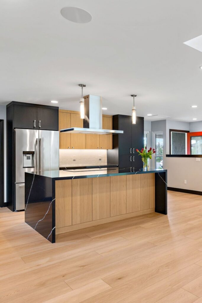 Open kitchen with wood-front island, black cabinetry, stainless refrigerator and light wood flooring