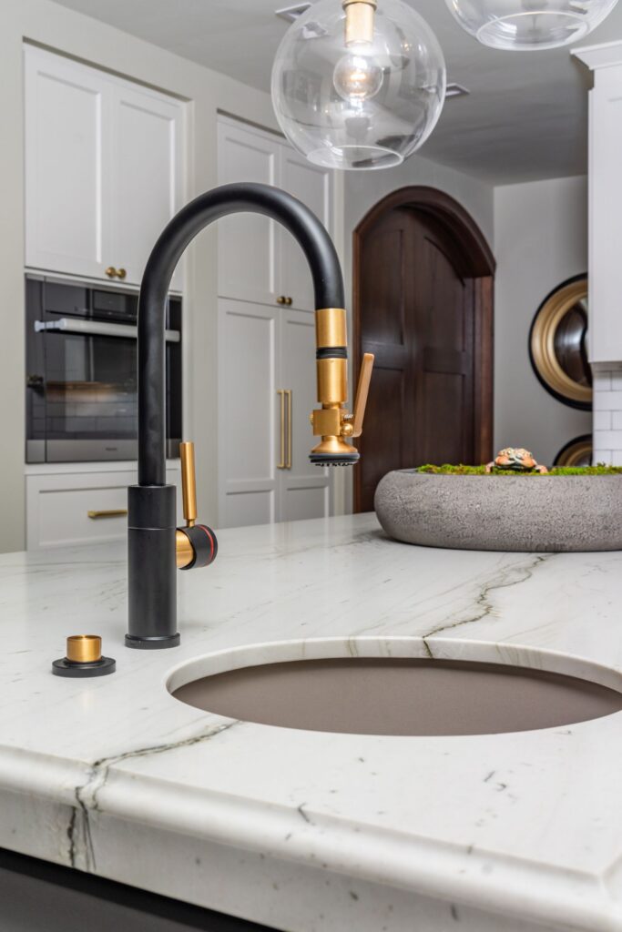 Black and brass prep faucet with round undermount sink, veined island countertop and clear globe pendants