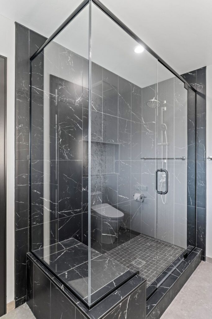 Glass-enclosed shower with black veined wall tile, recessed niche and handheld shower system