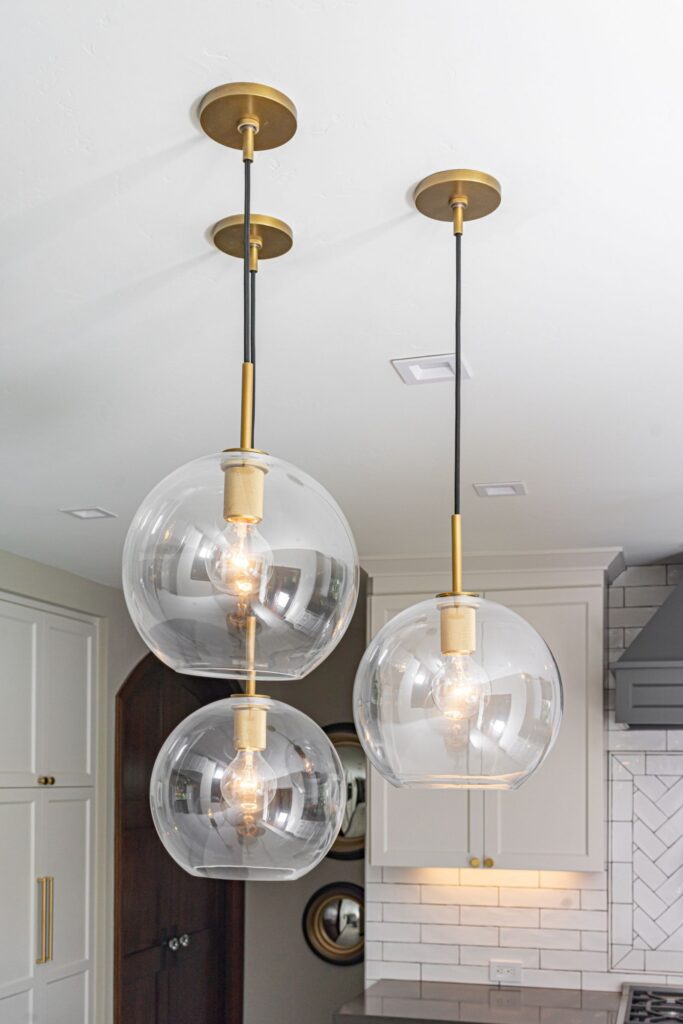 Three clear glass globe pendant lights with brass accents above the remodeled kitchen island