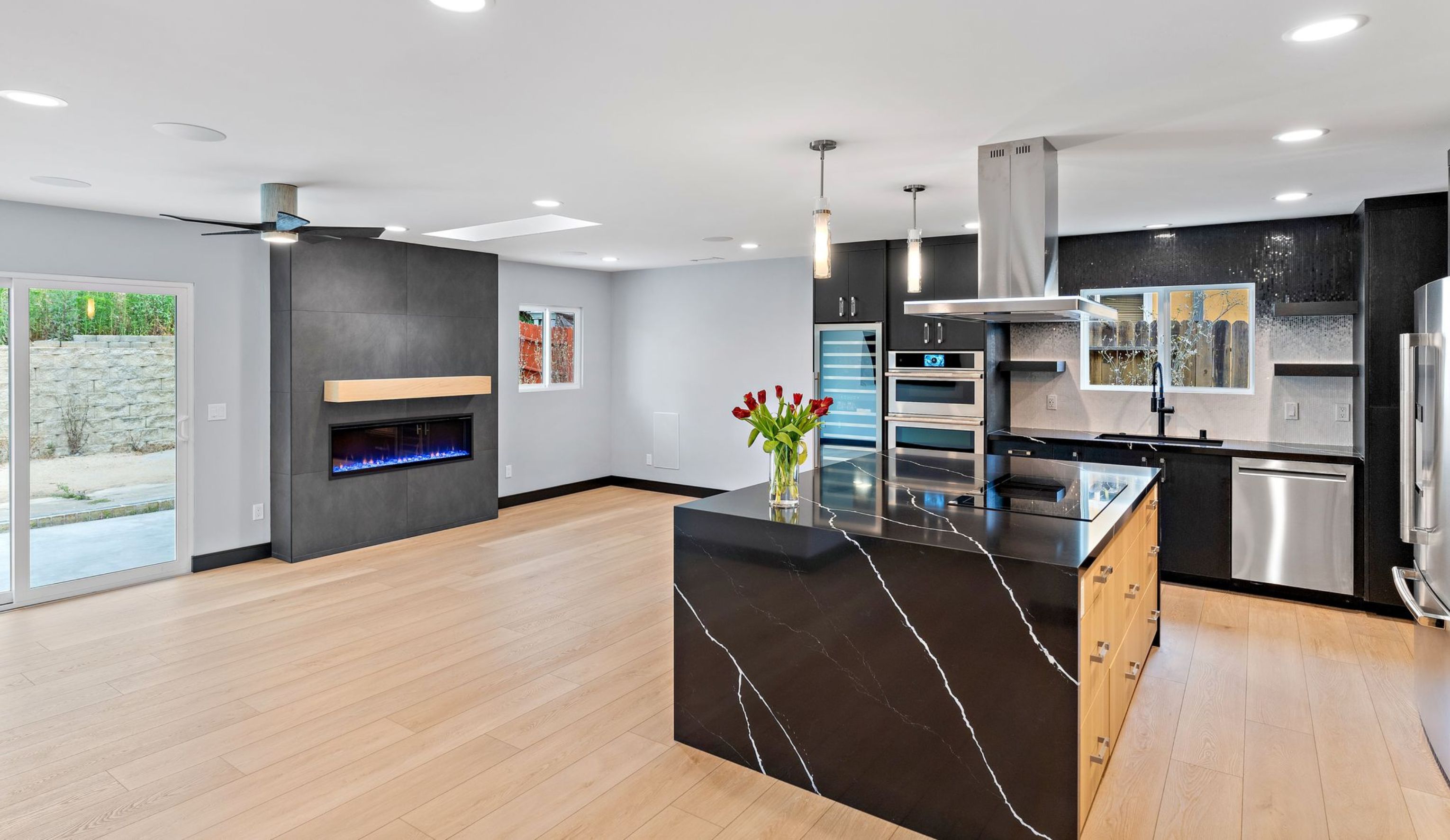 Open-concept San Diego kitchen and living room with black waterfall island, wood flooring and modern fireplace