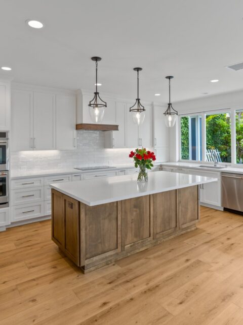 Ocean Beach whole-home remodel kitchen with white cabinetry, wood island, white counters, pendant lights and wood flooring.