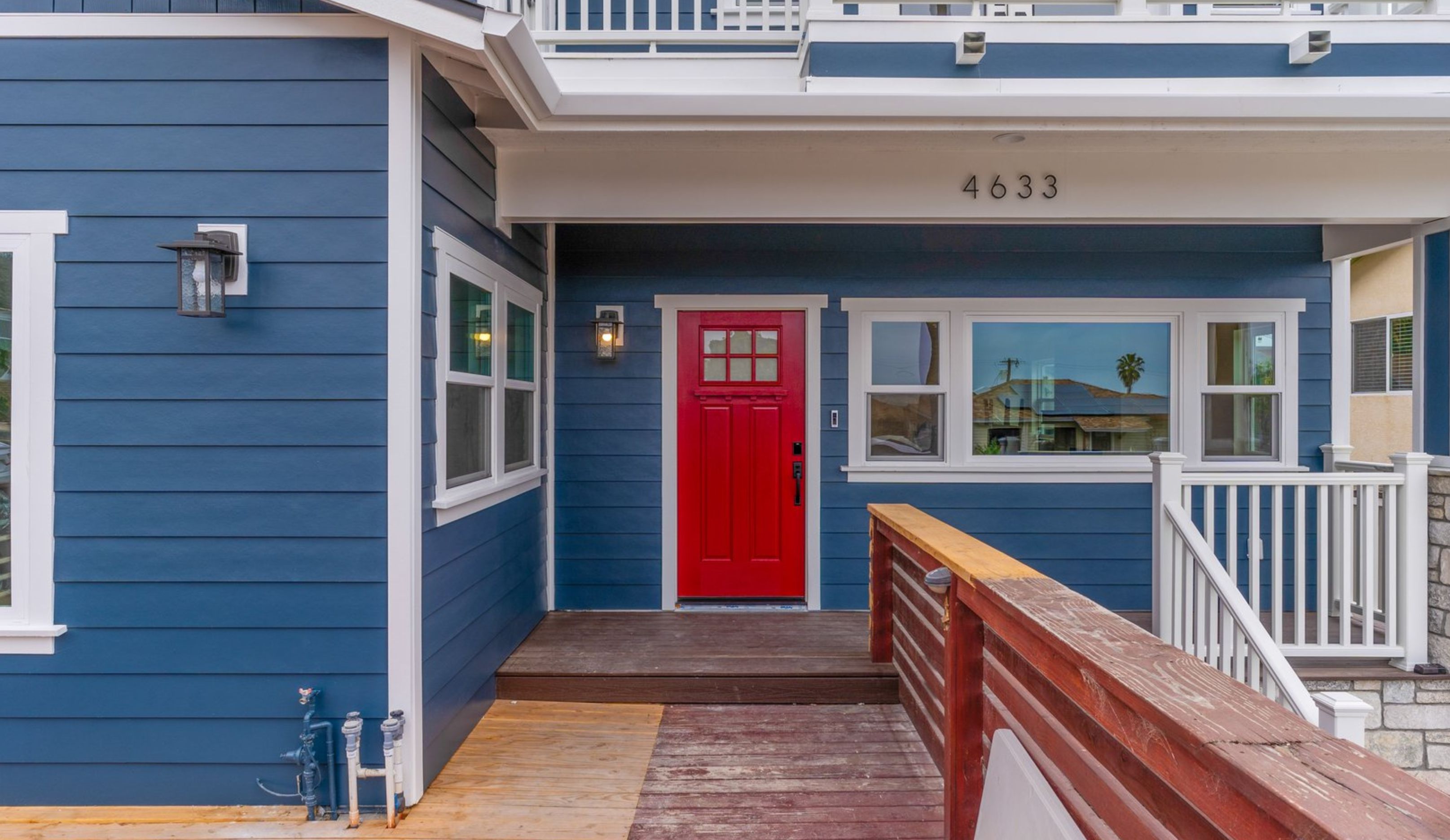 Ocean Beach remodeled home exterior with blue siding, red entry door, white trim, wood porch and second-floor balcony.