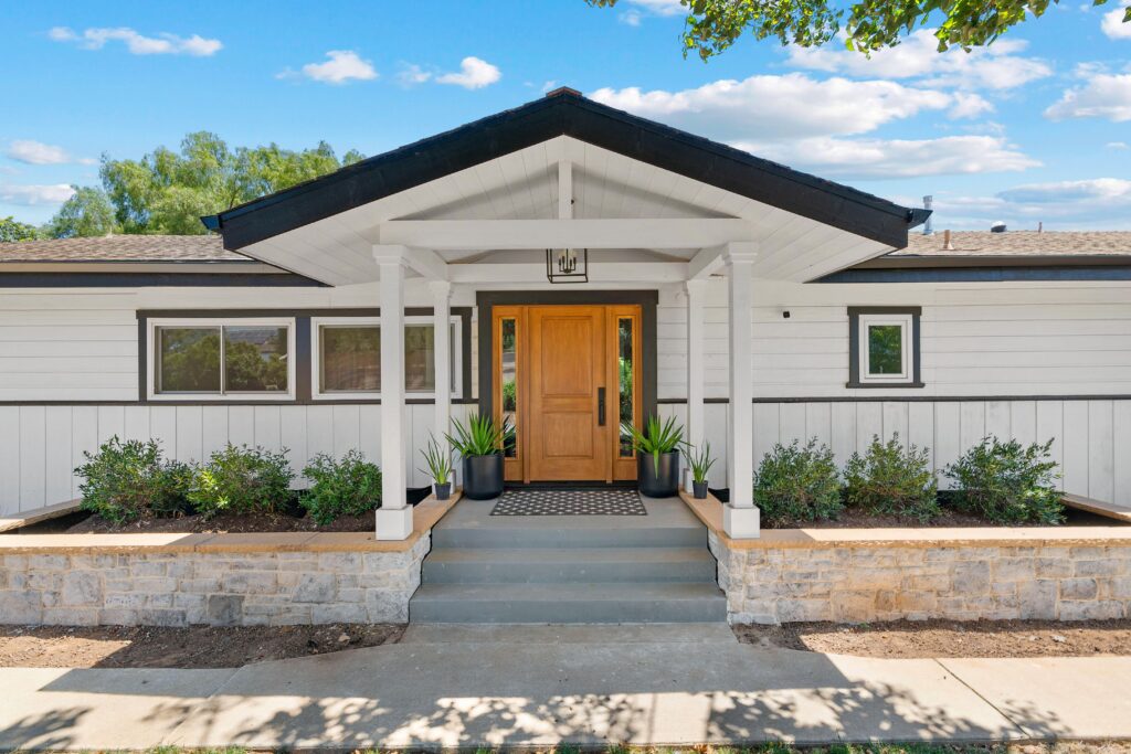 Front entry portico with gabled roof, white posts, wood door, black trim and stone planter walls