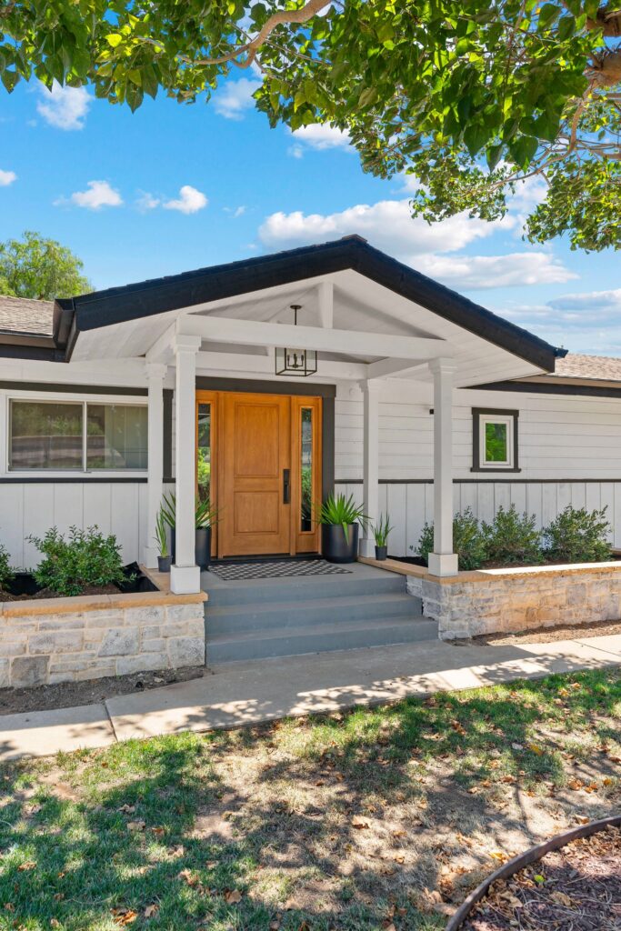Modern farmhouse entry with gabled portico, wood front door, black trim, white siding and stone planter walls