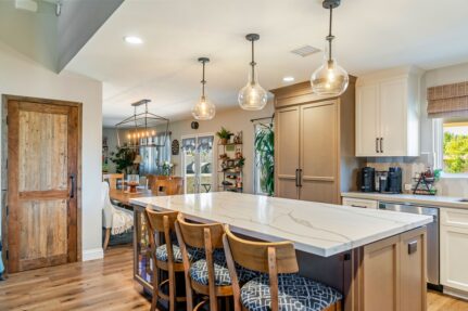 Kitchen with quartz waterfall island, glass pendant lights and reclaimed wood pantry door