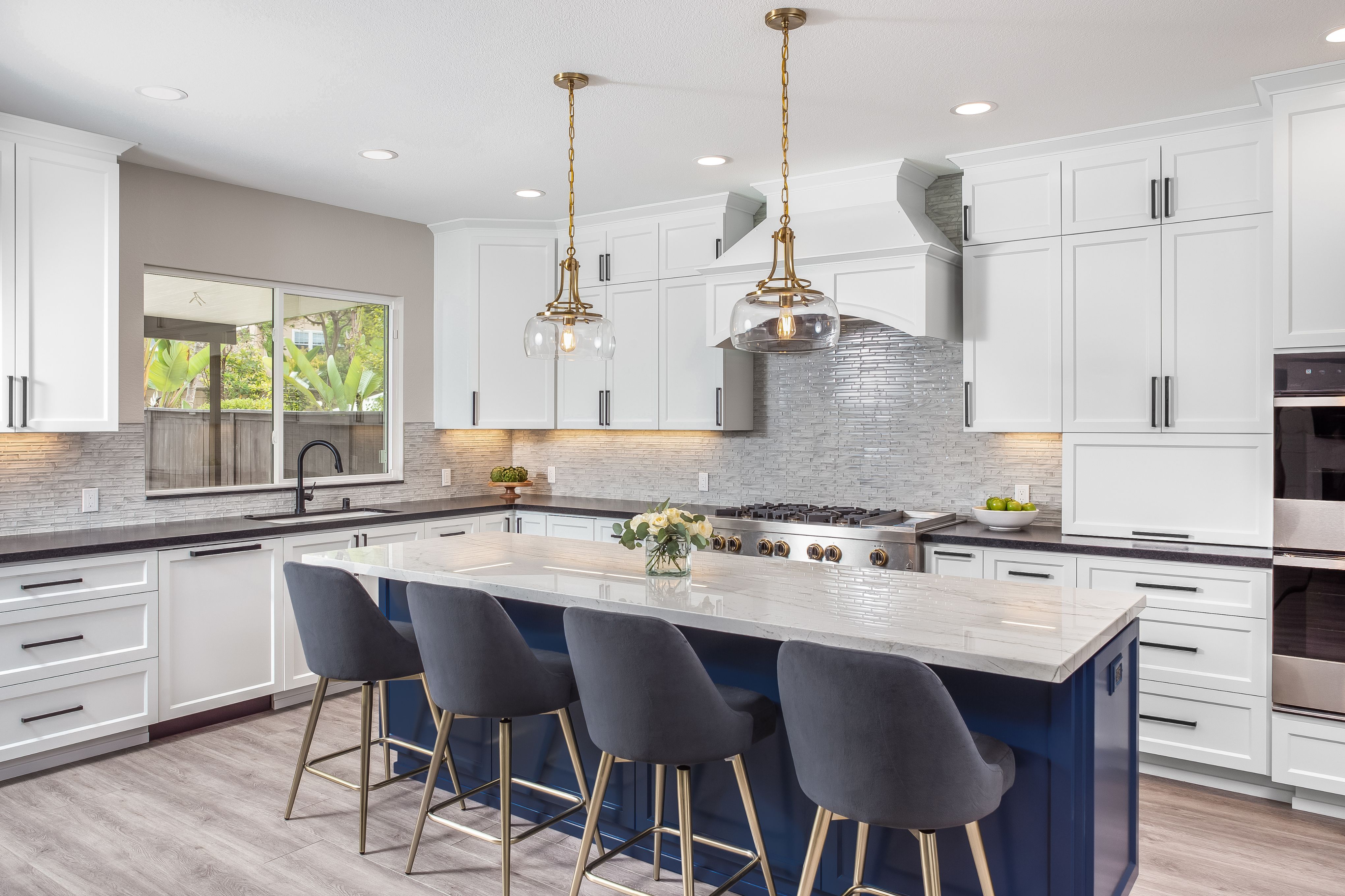 Kitchen remodel with white shaker cabinets, navy island, brass pendants and stainless range