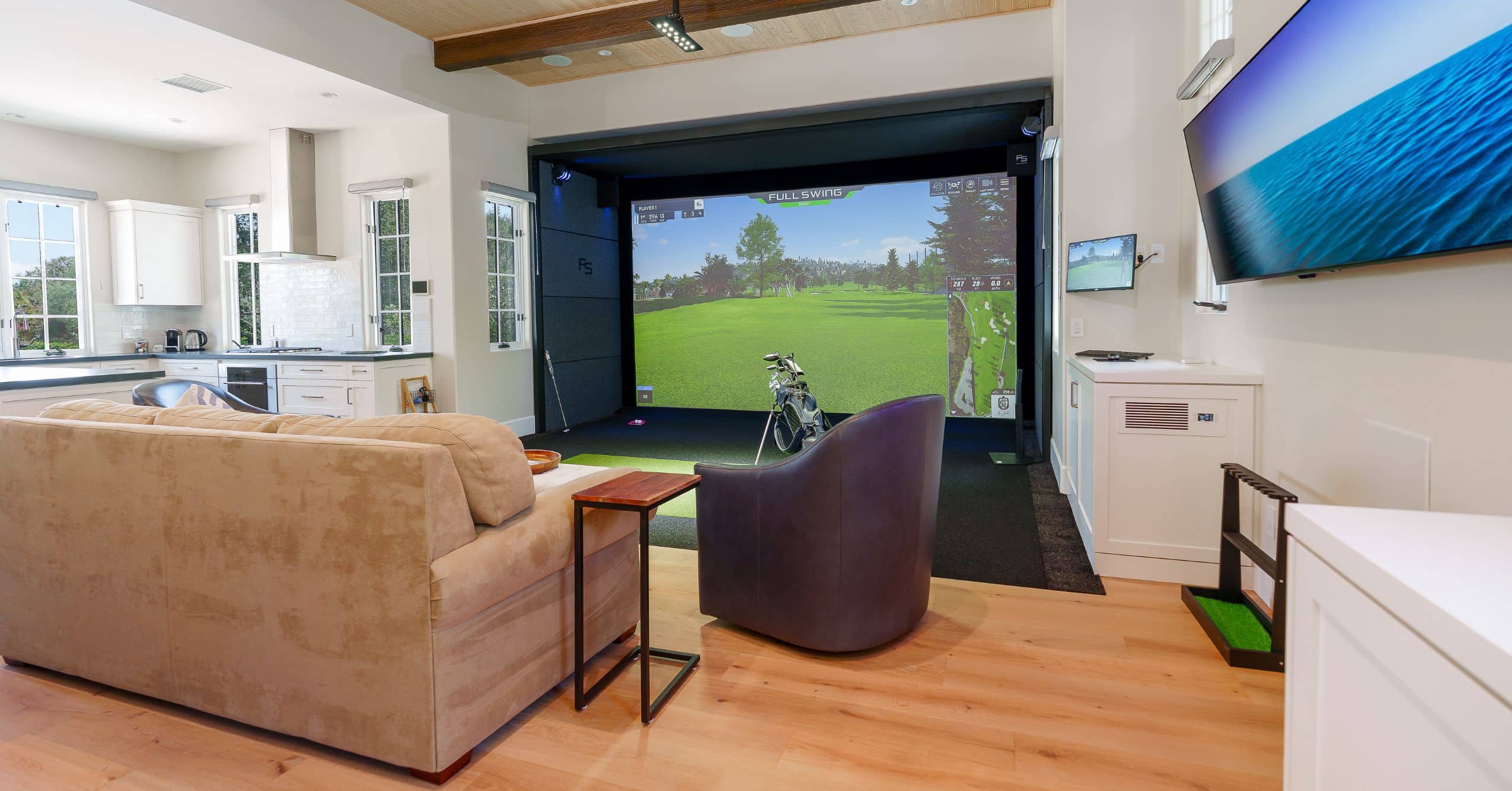 Attached ADU great room with golf simulator, seating area, wood flooring, and adjacent kitchen.