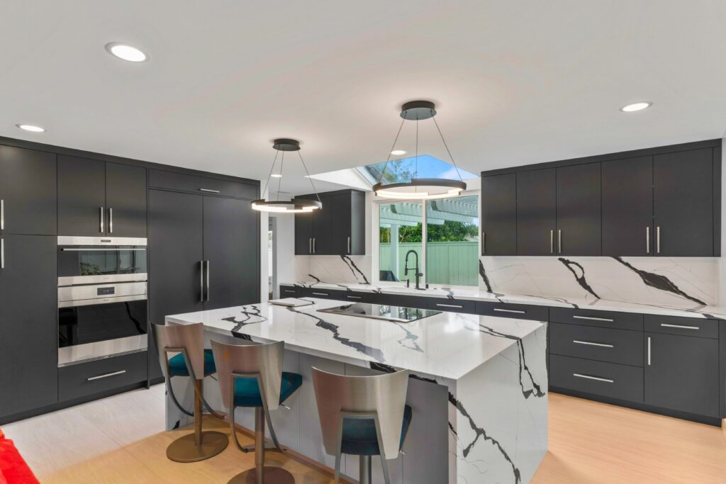 Modern kitchen with dark cabinetry, waterfall island, induction cooktop, slab backsplash and ring pendant lights.