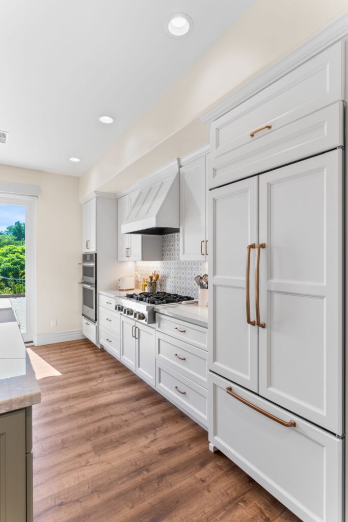 Kitchen with white cabinetry, paneled refrigerator, brass hardware, patterned backsplash and wood-look flooring.