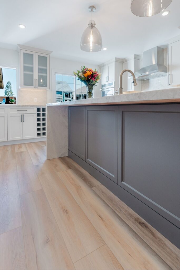 Two-tone kitchen with dark island, white cabinetry, pendant lights, stone counters and built-in wine storage.