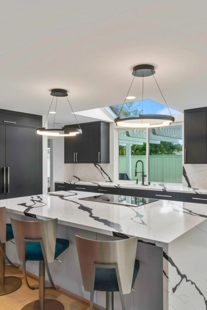 Modern San Diego kitchen with waterfall island, dark cabinetry, skylight, pendant lights and counter seating.