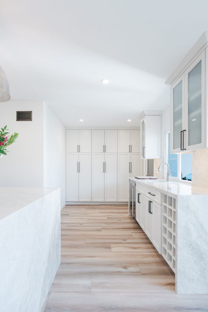 Kitchen pantry and beverage area with tall white cabinets, glass-front uppers, wine cubbies and waterfall counter.