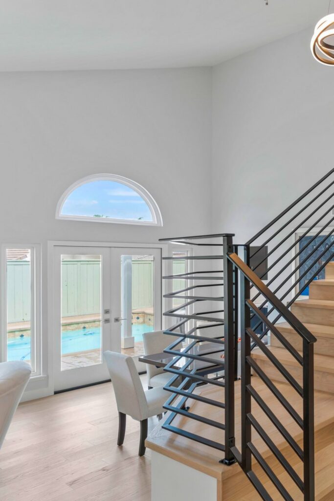 Staircase with black horizontal railing, light wood treads, French doors and arched transom window.