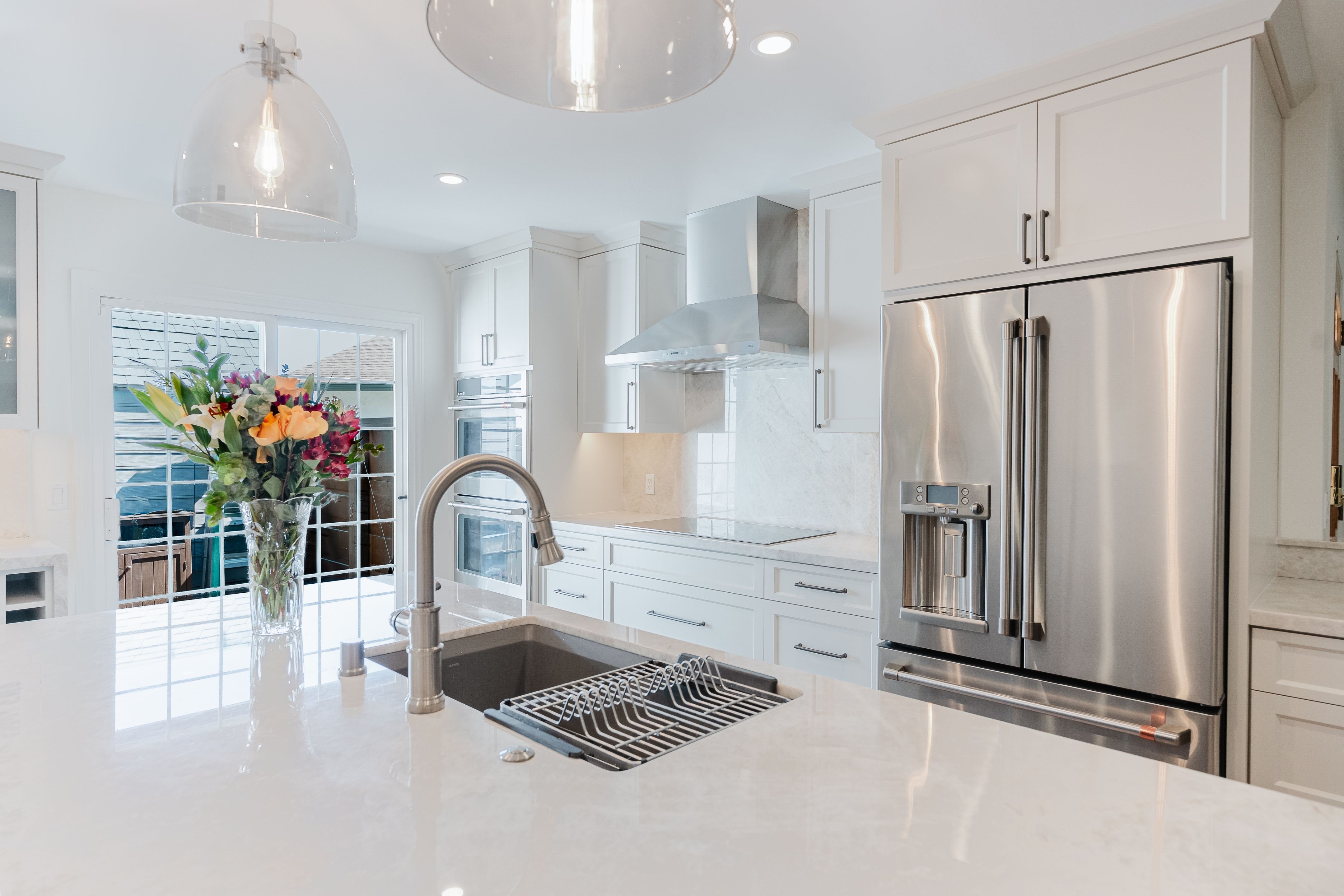 Remodeled kitchen with large sink island, white cabinetry, stone counters, stainless appliances and glass pendant lights.