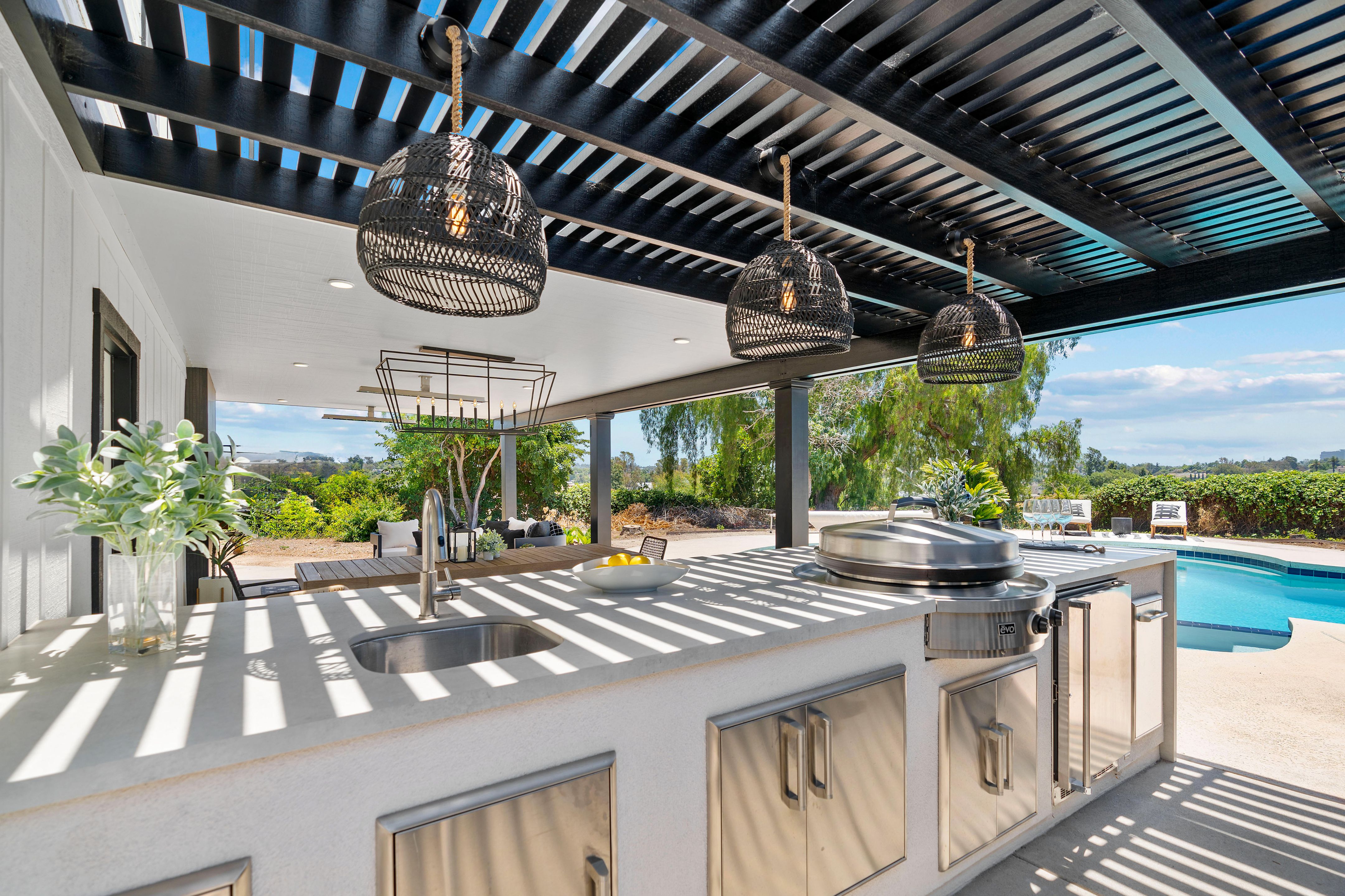 Outdoor kitchen with stainless cabinetry, built-in Evo cooktop, sink, quartz counter and black slatted trellis