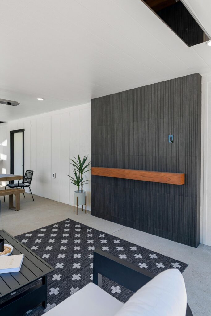 Covered outdoor lounge with dark vertical fireplace wall, wood mantel, white ceiling and recessed lighting