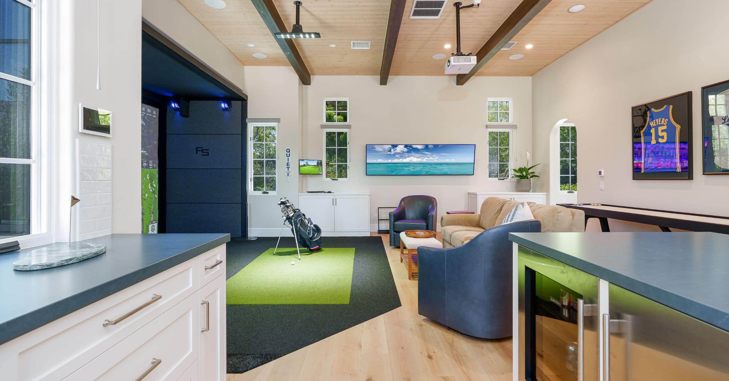 Spacious ADU great room with indoor golf simulator, lounge seating, built-in cabinetry, and wood-beam ceiling.