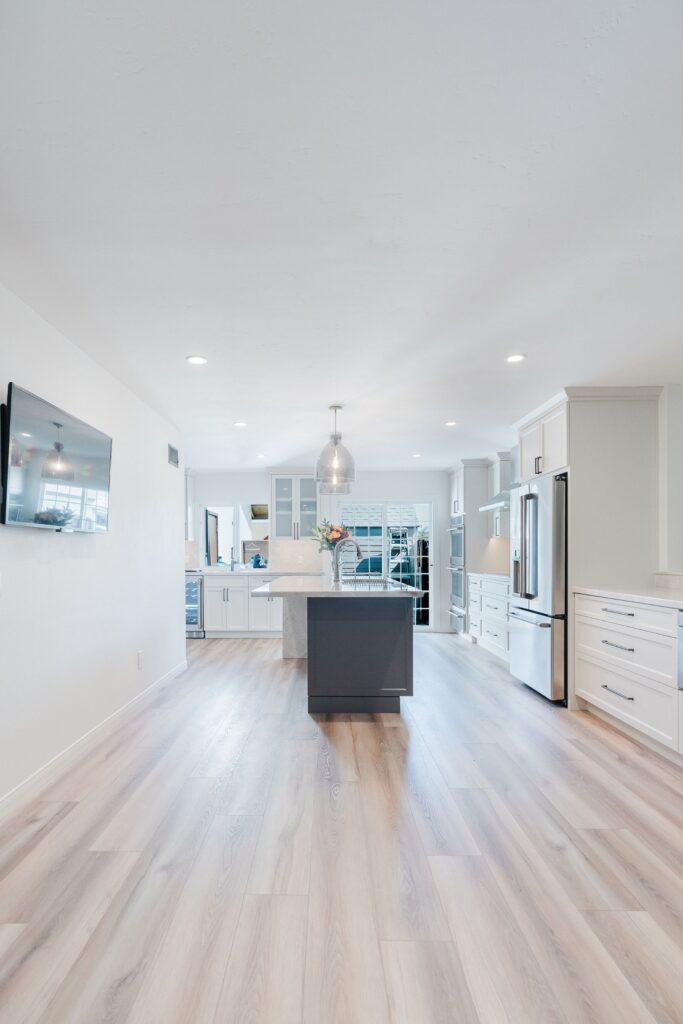 Open kitchen with centered island, white cabinetry, stainless refrigerator, pendant lights and continuous wood-look flooring.