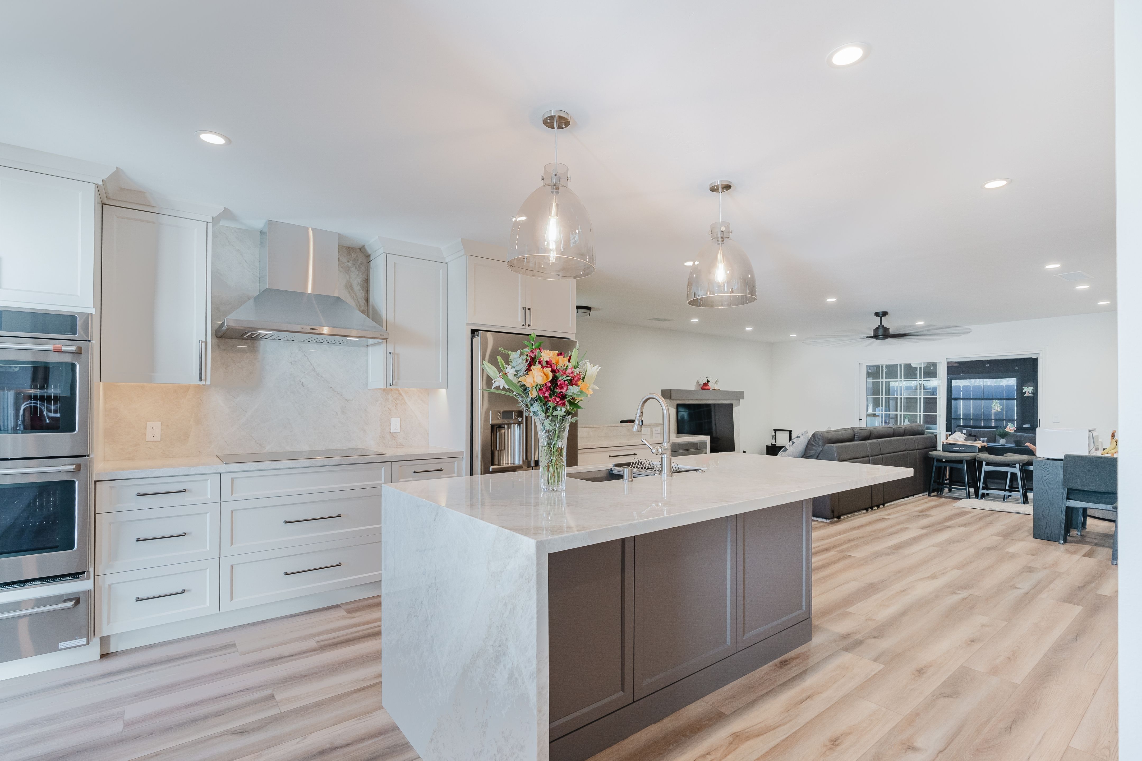 Open-concept kitchen and living room with waterfall island, two-tone cabinetry, pendant lights and wood-look flooring.