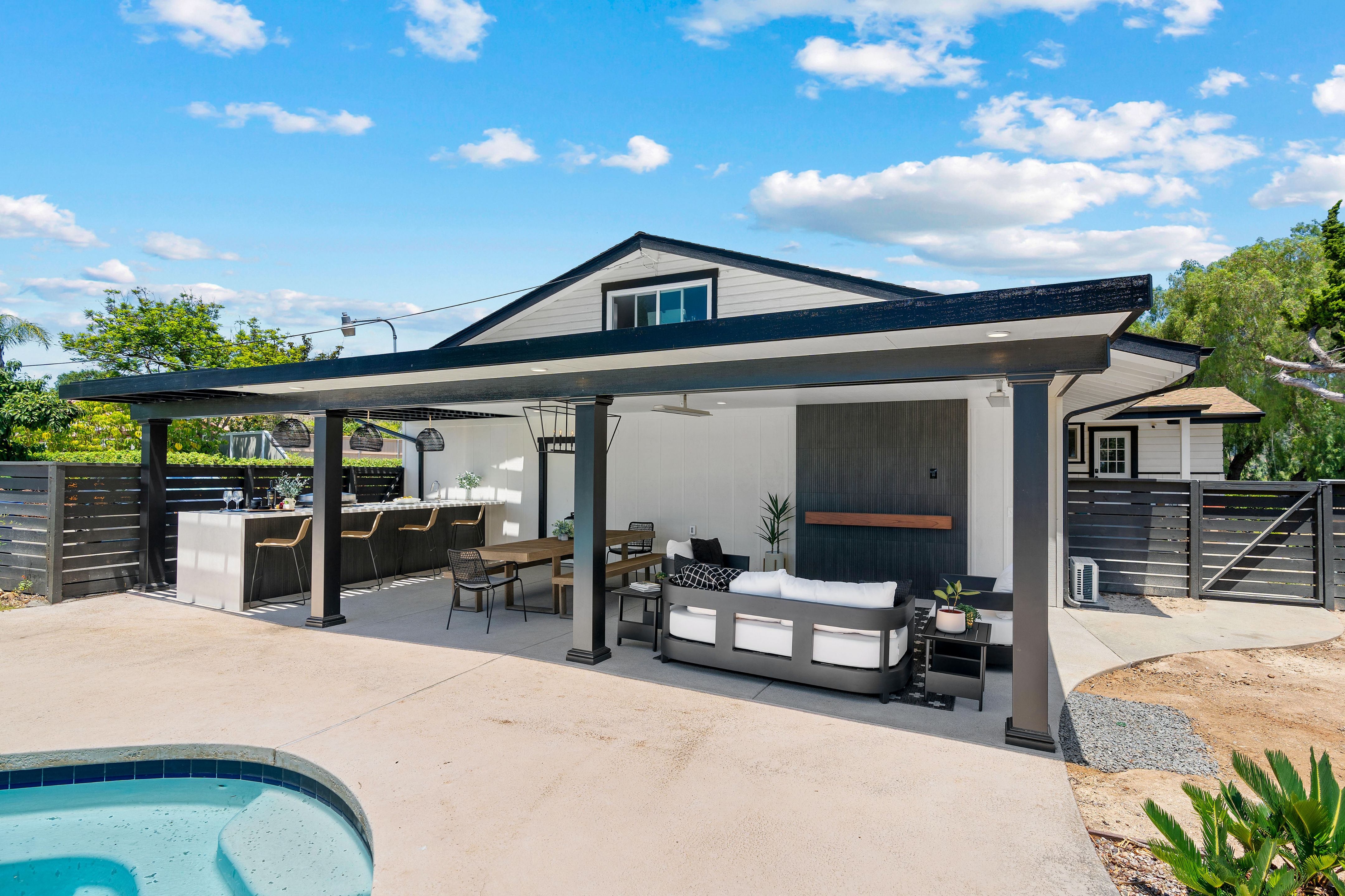 Covered outdoor living area with kitchen bar, dining table, lounge seating, black columns and pool