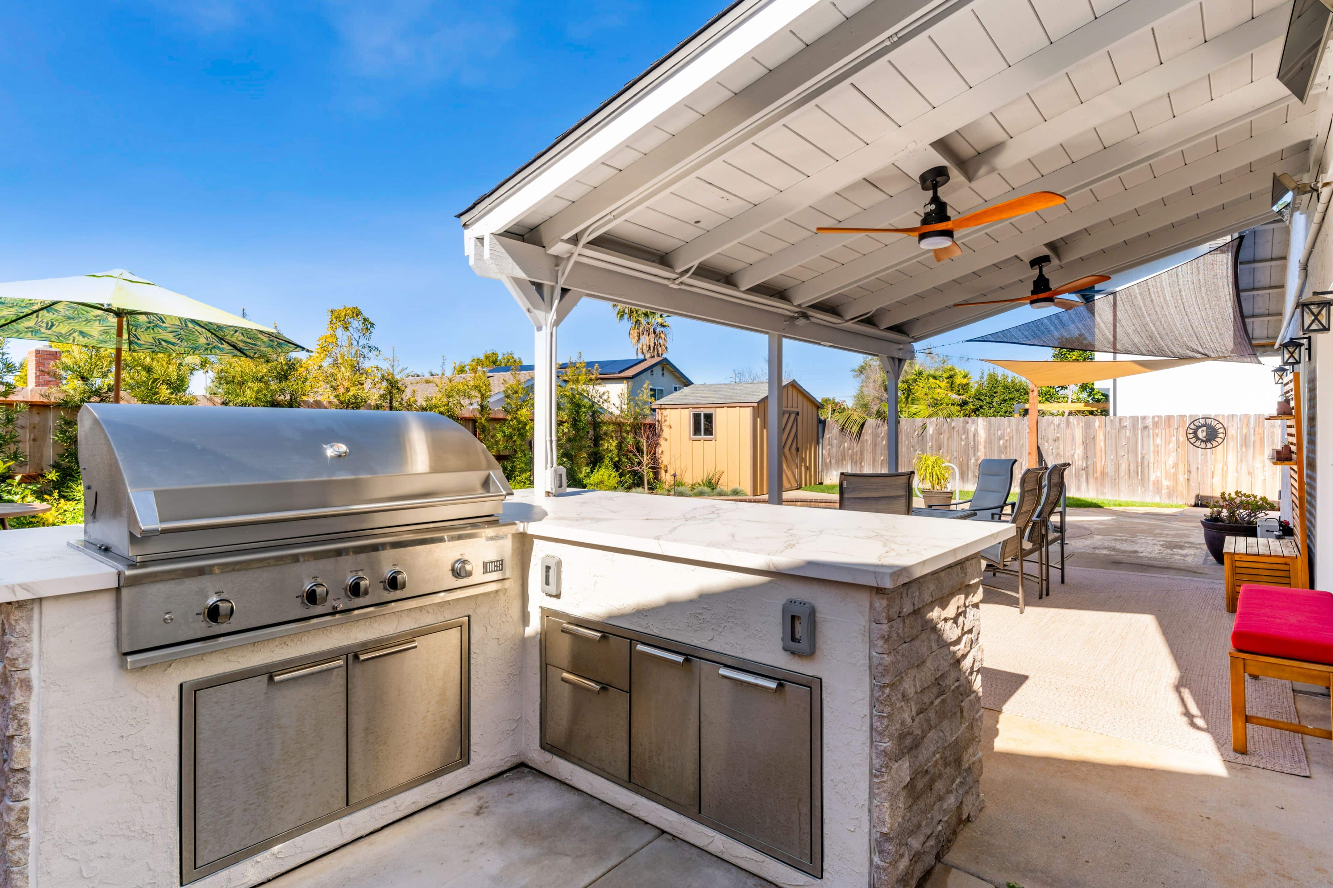 Outdoor kitchen with built-in stainless grill, stone-clad counter and covered patio