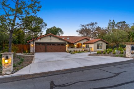 Street-view of Spanish-style home with tile roof, reworked garage doors, stone driveway pillars and paver inlay