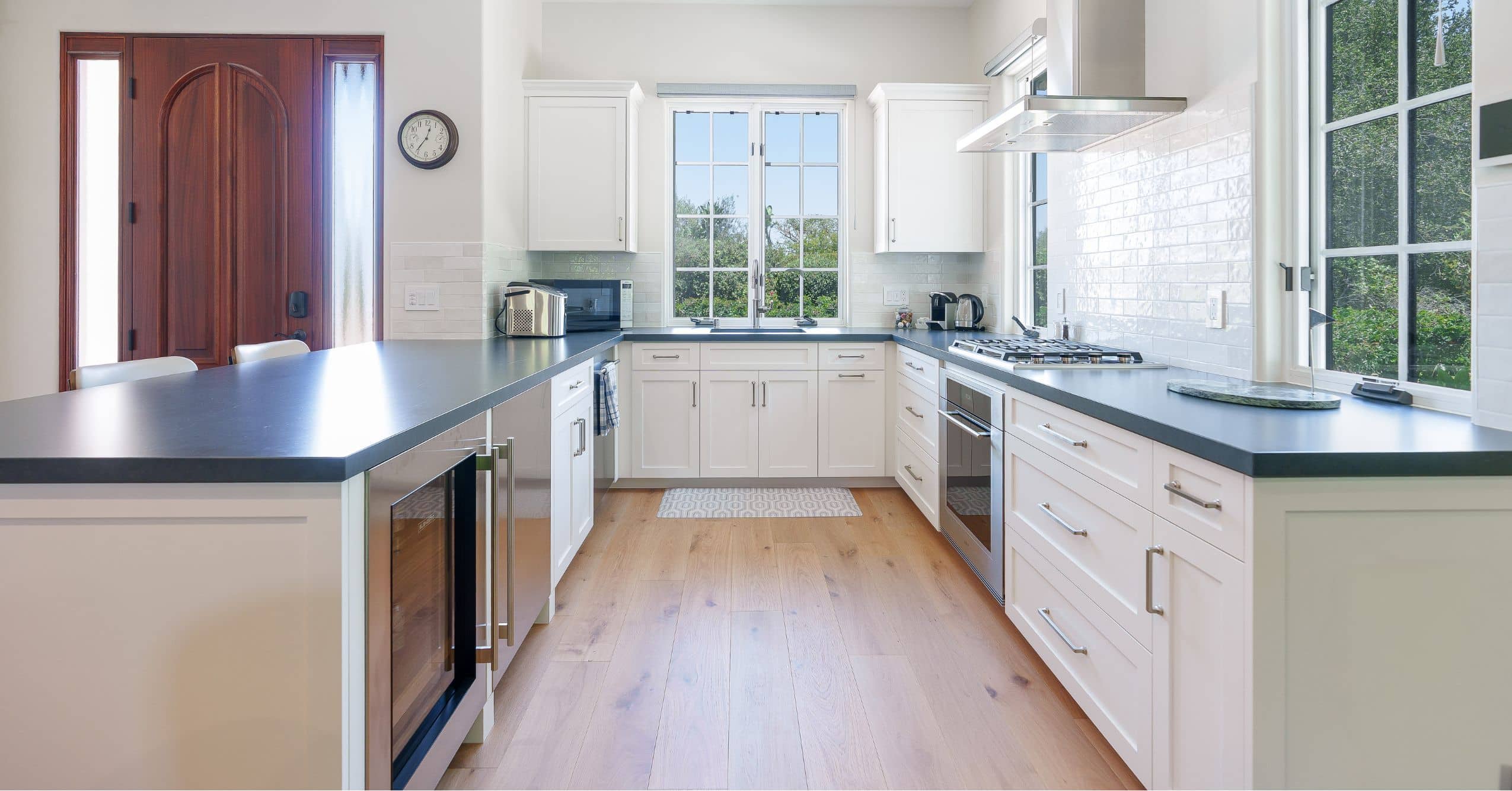 Bright ADU kitchen with white cabinetry, dark countertops, stainless steel appliances, and wood flooring.
