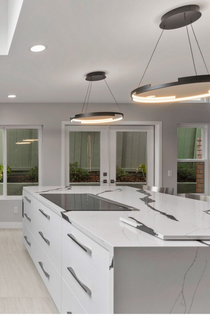 Kitchen island with induction cooktop, bold veined countertop, ring pendants and French doors to the patio.